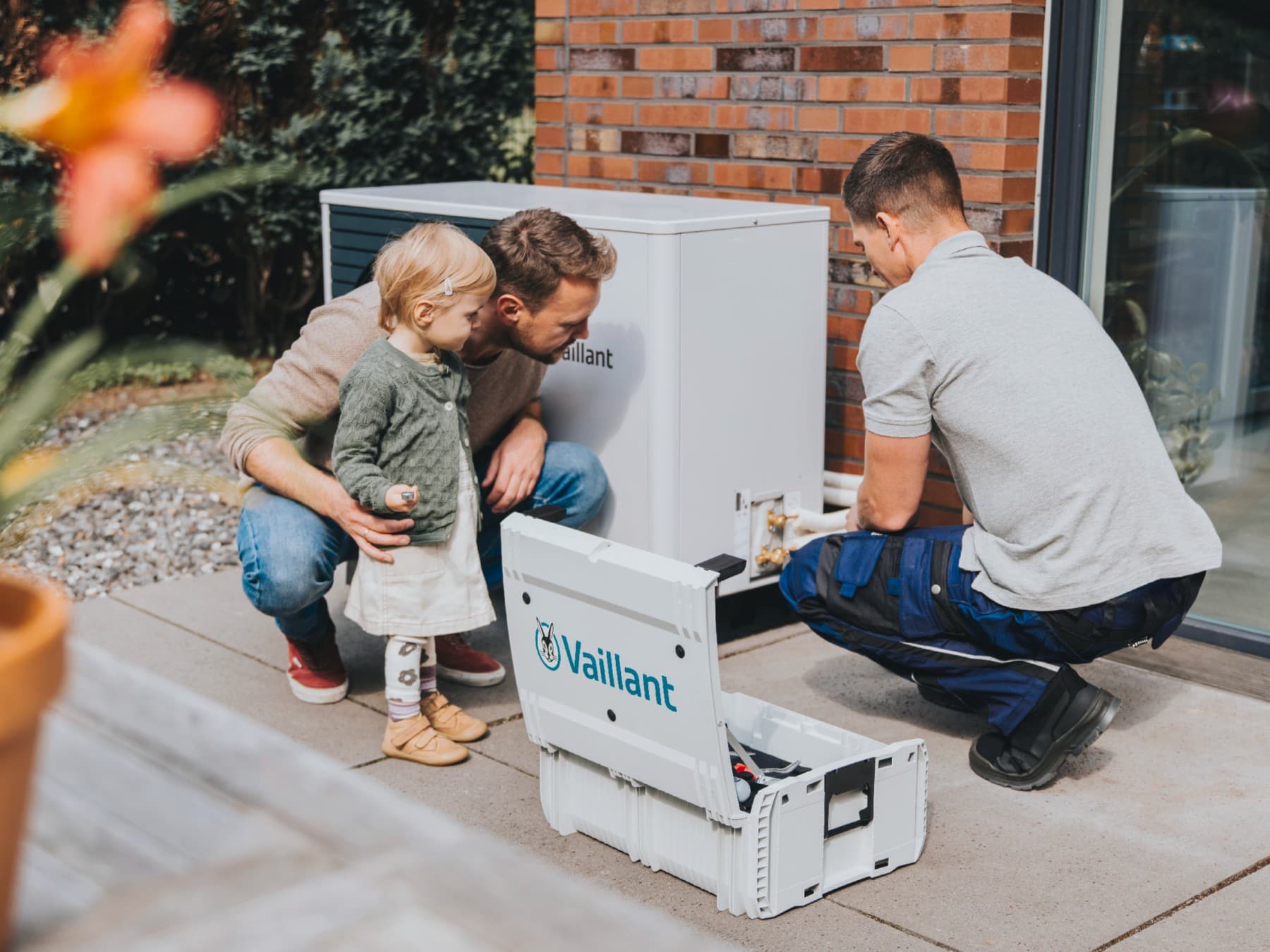 Otac i njegova kćerka gledaju instalatera kako instalira toplotnu pumpu